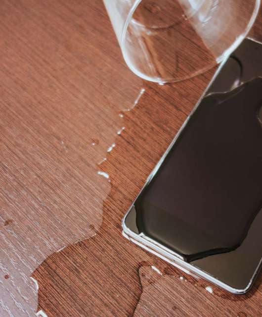 Smartphone on a table covered with water next to a spilled cup of water.