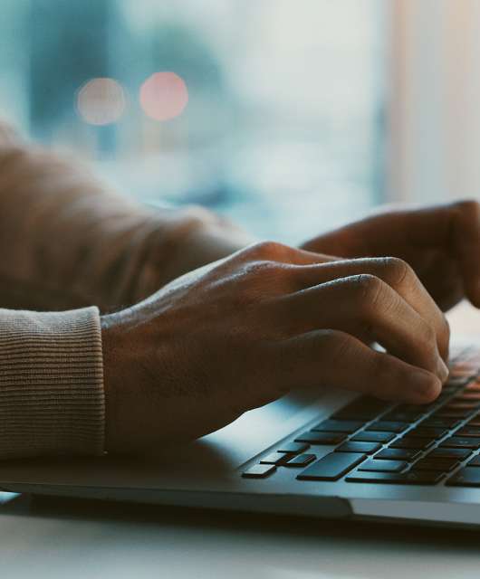 Two hands hovering over a laptop keyboard.