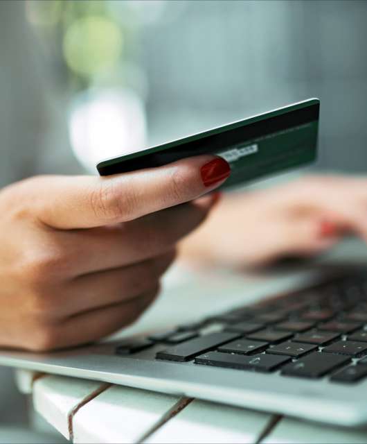 Hand holding a credit card next to a laptop.